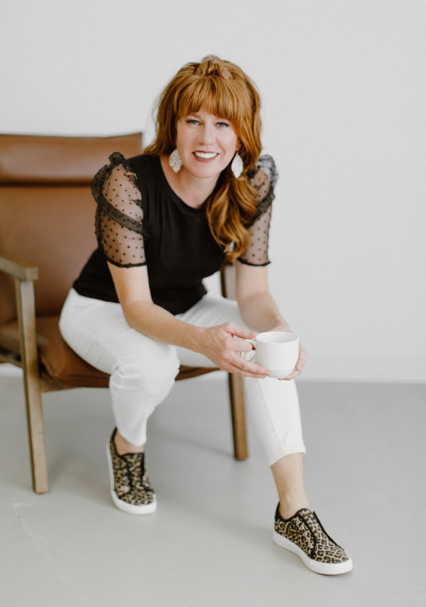 Kathryn Kurtz of K Squared Design Studio sits on a chair with a cup of coffee friendly smiling 